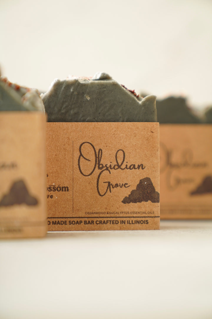 Obsidian Grove soap bars in kraft paper wrap, row of bars with dark grey tops