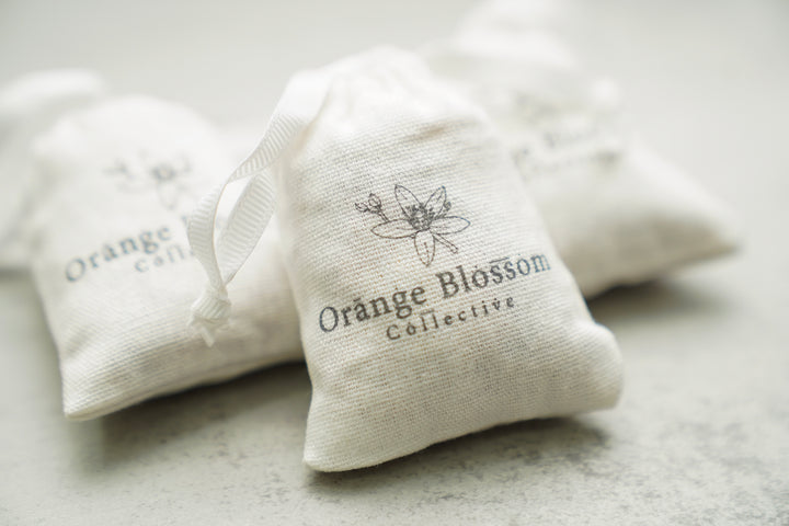 Orange Blossom Collective scented sachets in muslin drawstring bags, standing upright on a light surface