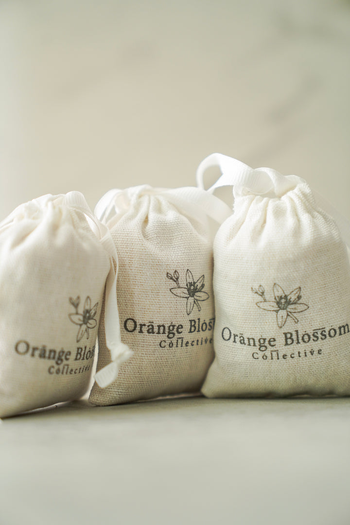 Orange Blossom Collective linen scent sachets with logo print, available in Cashmere Musk, Orange Blossom, Olive Branch, and Jasmine