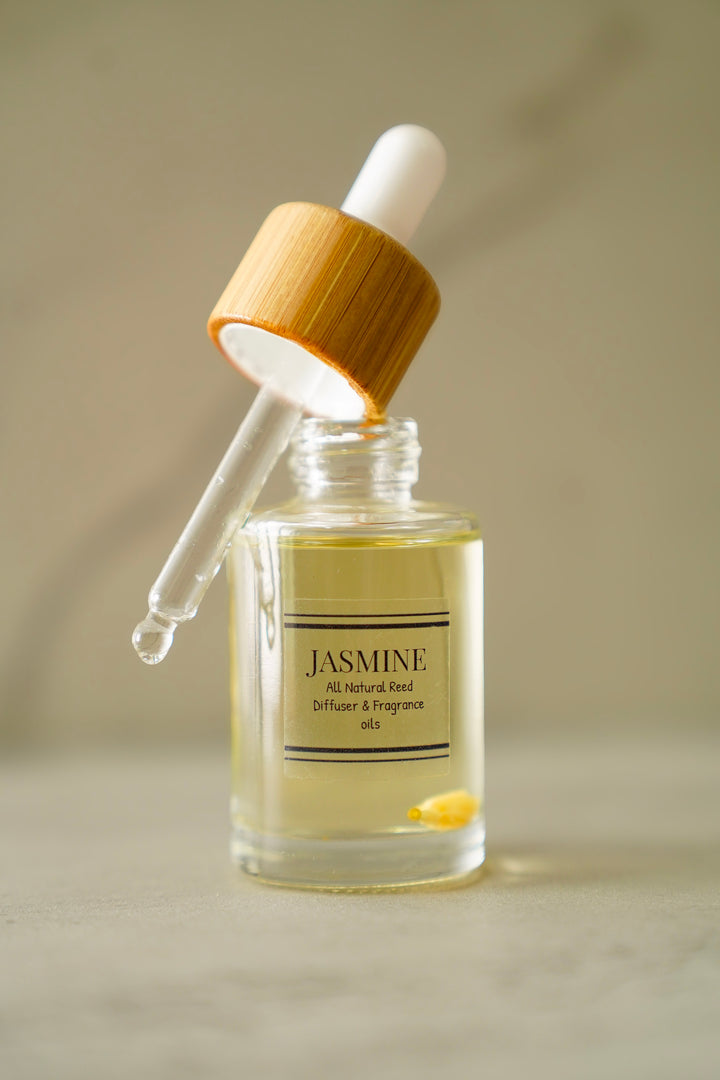 A clear glass dropper bottle labeled 'JASMINE' with pale yellow liquid inside, topped with a white dropper and a light wood cap, set against a soft beige background.