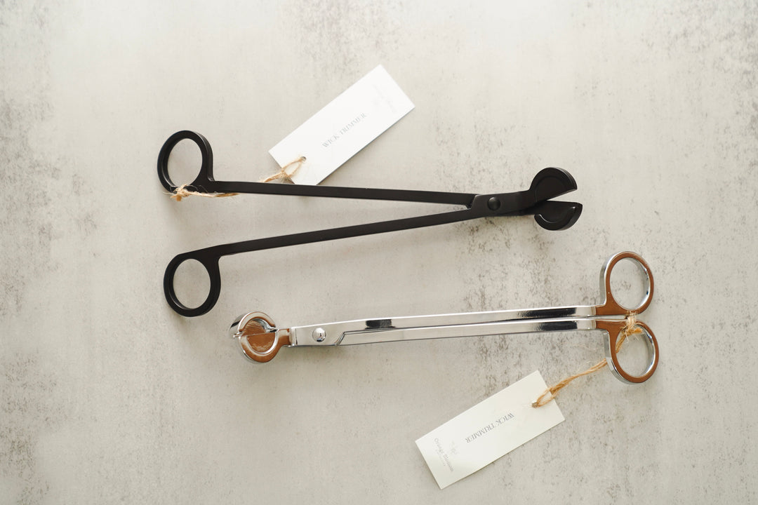 Silver and black scissor-style wick trimmer with brand tag on a marble surface